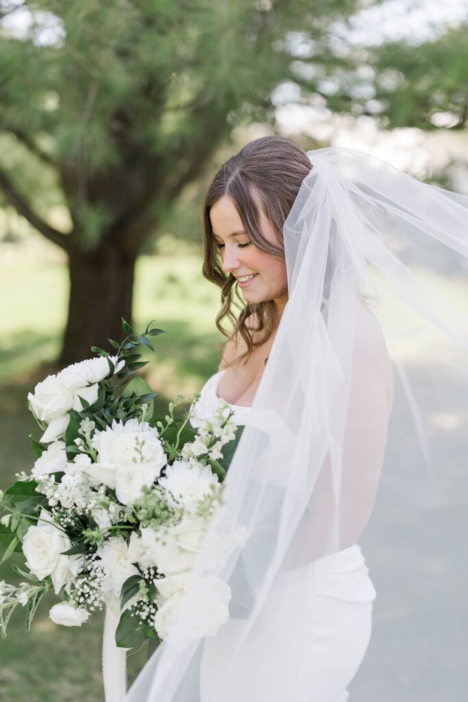 Bride smiling while holding a lush white bouquet during her Mill Pond Event Center wedding in Northern Michigan.