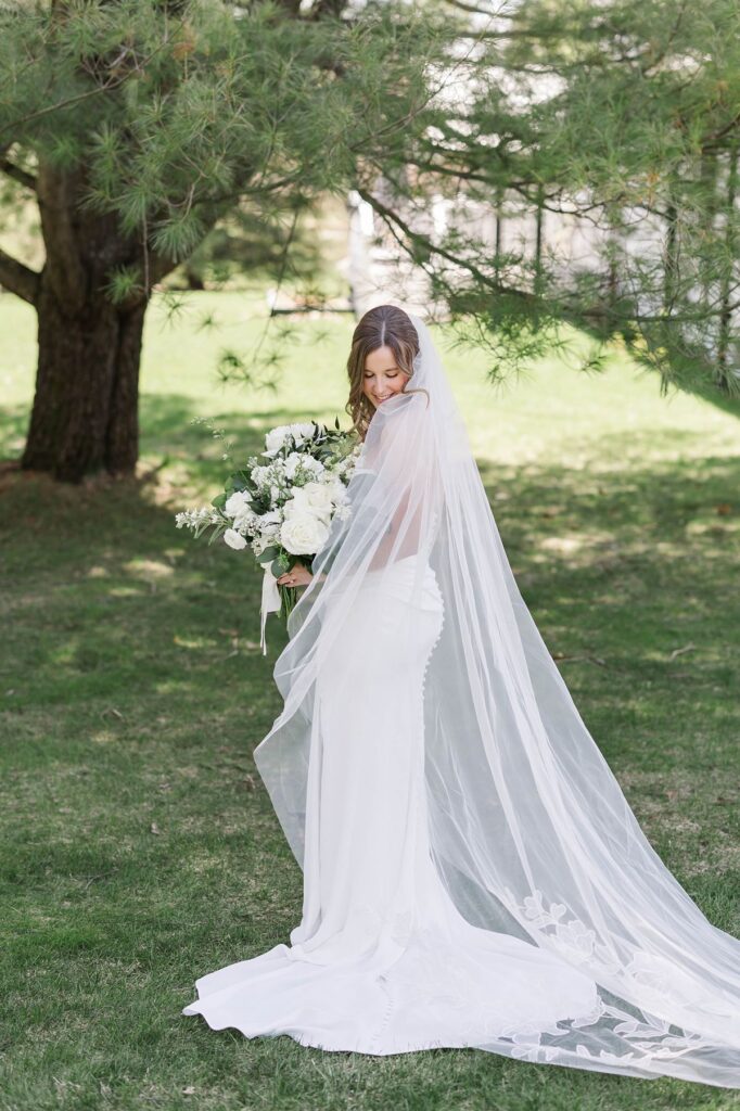 Bride in a timeless wedding gown with a flowing cathedral veil and white bouquet at Mill Pond Event Center in Kalkaska, Michigan.