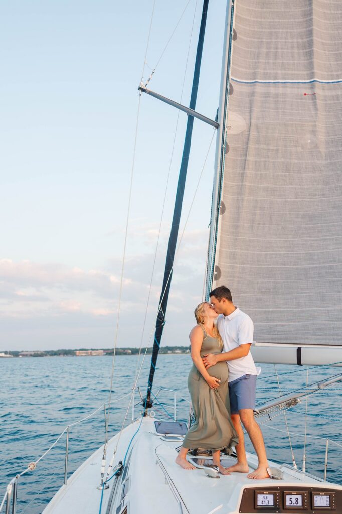 Couple embracing on the bow of a sailboat during a sunset Traverse City sailboat photos session on Grand Traverse Bay