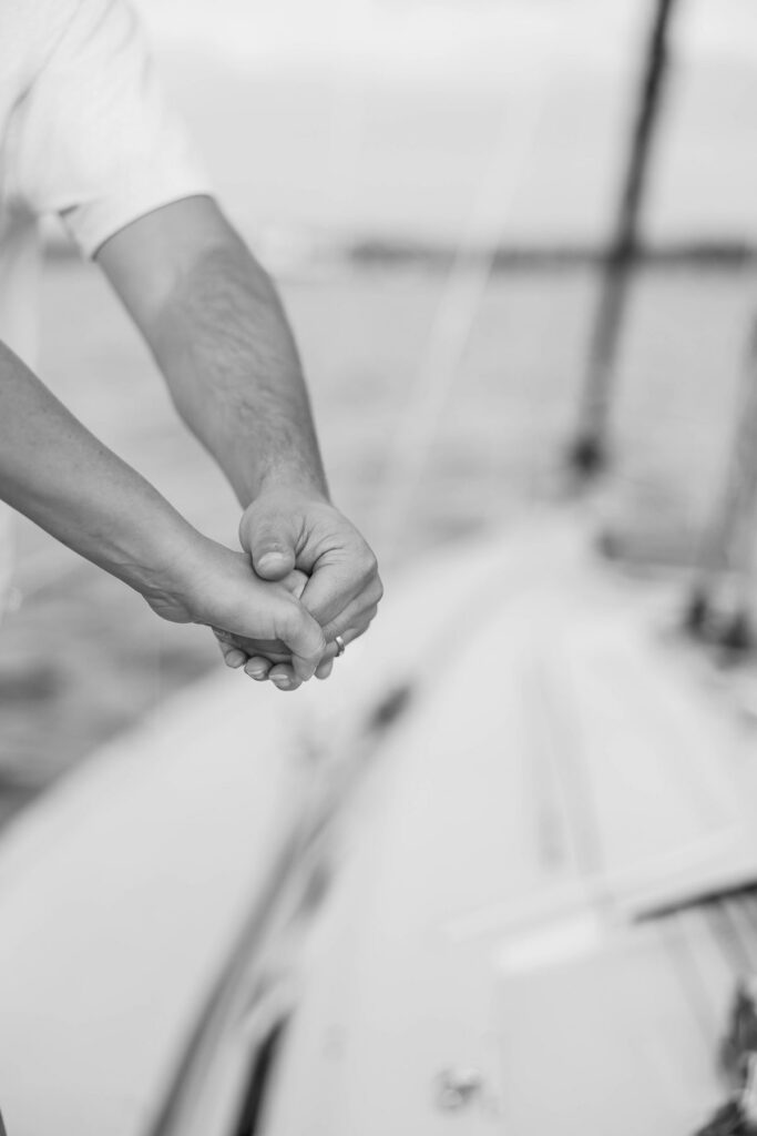 Close-up of a couple holding hands aboard a sailboat during a Traverse City sailboat photos session on Grand Traverse Bay