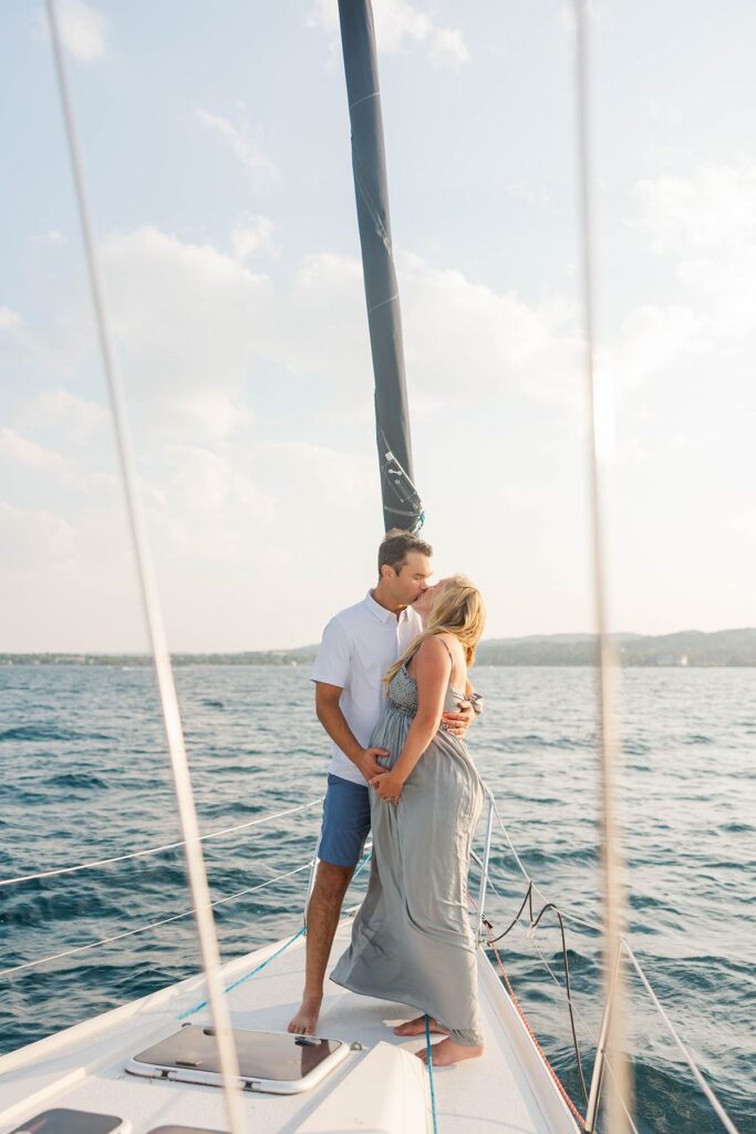 Couple embracing on the bow of a sailboat during a sunset Traverse City sailboat photos session on Grand Traverse Bay