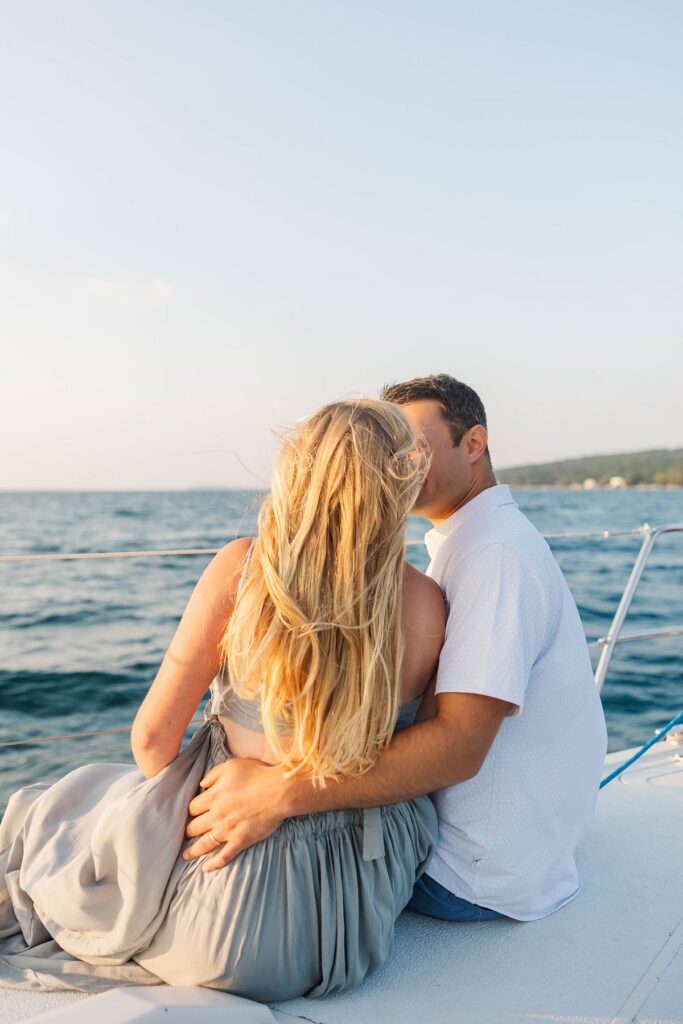 Couple embracing aboard a sailboat during a sunset Traverse City sailboat photos session on Grand Traverse Bay