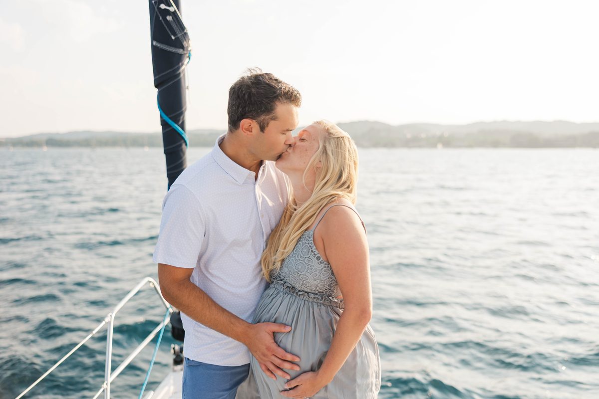 Couple kissing on a sailboat during a sunset Traverse City sailboat photos session on Grand Traverse Bay