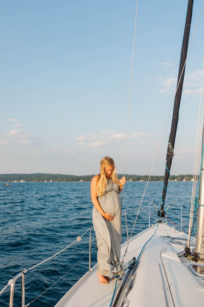 Mother-to-be on the bow of a sailboat during a sunset Traverse City sailboat photos session on Grand Traverse Bay