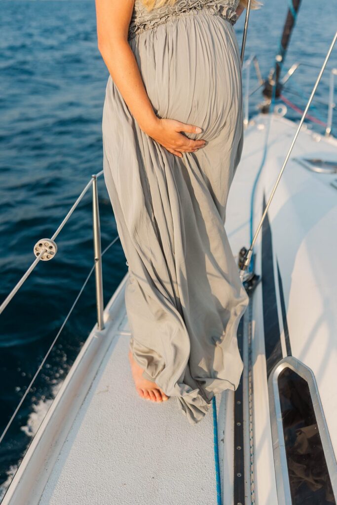 Close-up of a baby bump aboard a sailboat during a sunset Traverse City sailboat photos session on Grand Traverse Bay