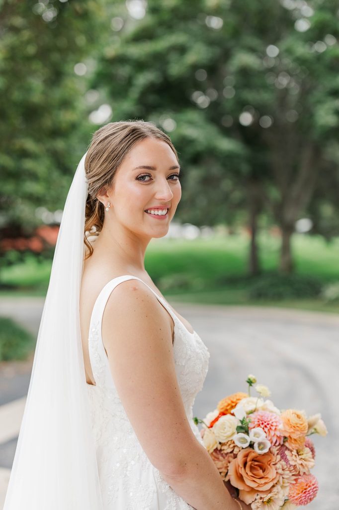 Natural bridal portrait of Allison smiling in her wedding dress and veil with greenery behind her at Black Star Farms in Suttons Bay, Michigan.