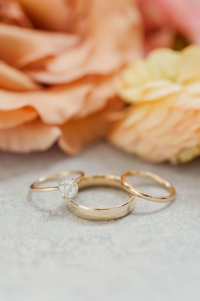 Allison and Cole's gold wedding rings displayed beside peach-colored flowers during their intimate Northern Michigan wedding.