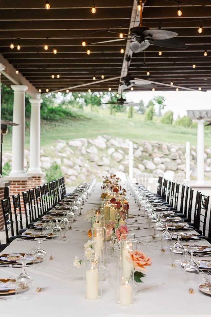 Long wedding reception table decorated with colorful florals and candles beneath string lights on the covered patio at Black Star Farms winery.