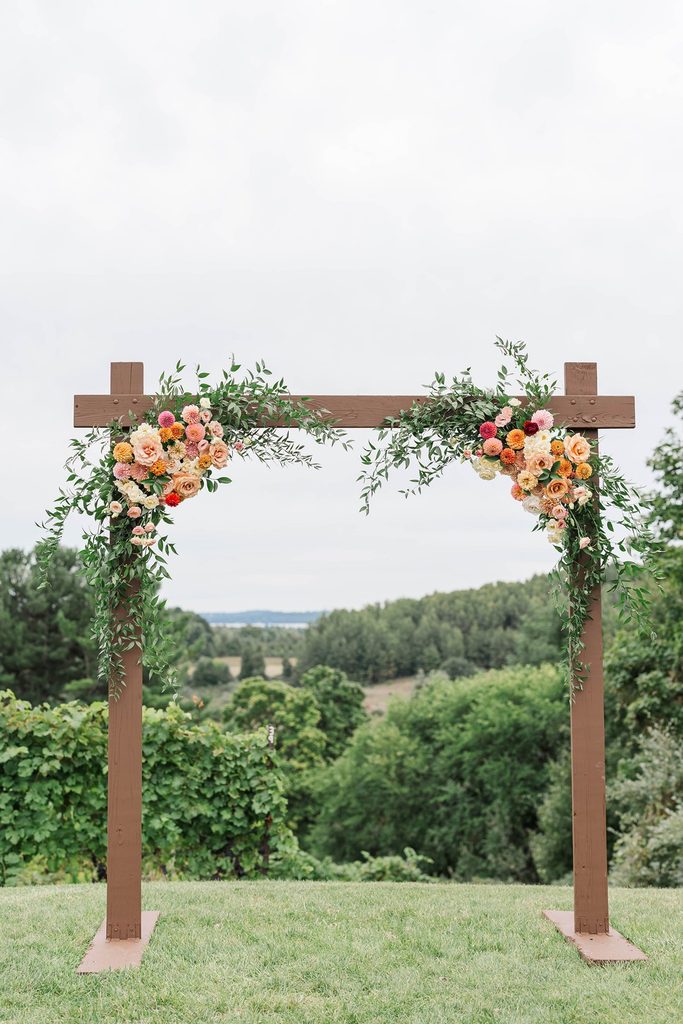 Wooden wedding ceremony arbor decorated with colorful florals overlooking the vineyards at Black Star Farms in Suttons Bay, Northern Michigan.