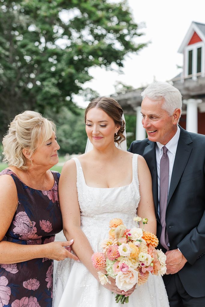 Allison smiling with her mother and father outside Black Star Farms during a special family moment before her wedding ceremony.
