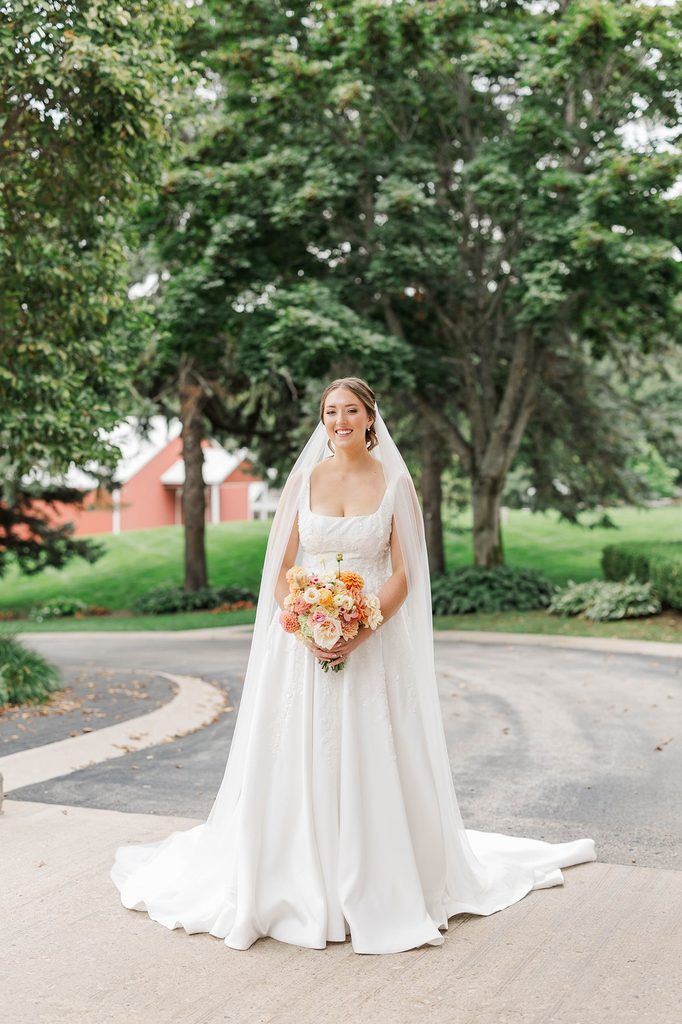 Full-length bridal portrait of Allison wearing her elegant white wedding gown and veil while holding a colorful bouquet at Black Star Farms in Northern Michigan.