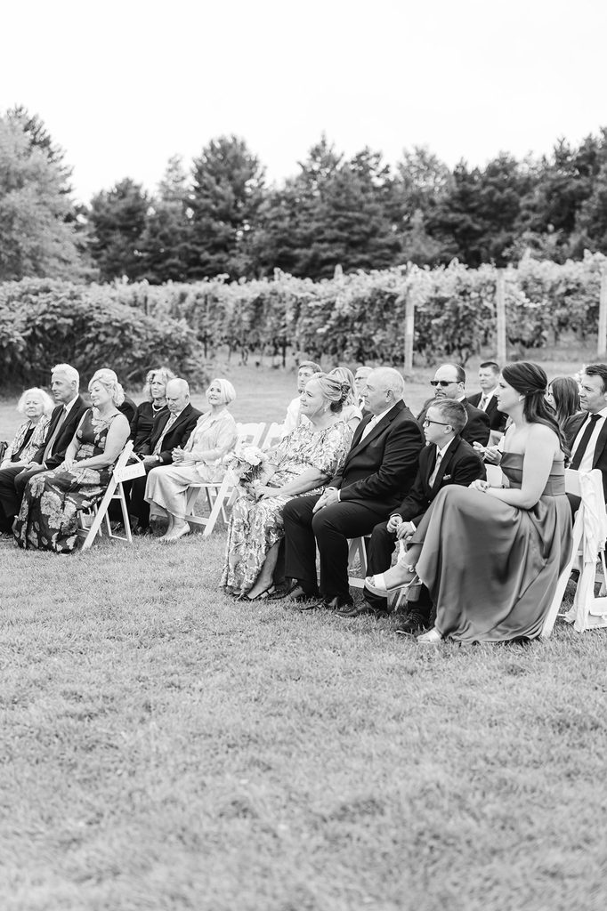 Black-and-white photograph of guests seated beside the vineyard during Allison and Cole's intimate 38-person Black Star Farms wedding ceremony.
