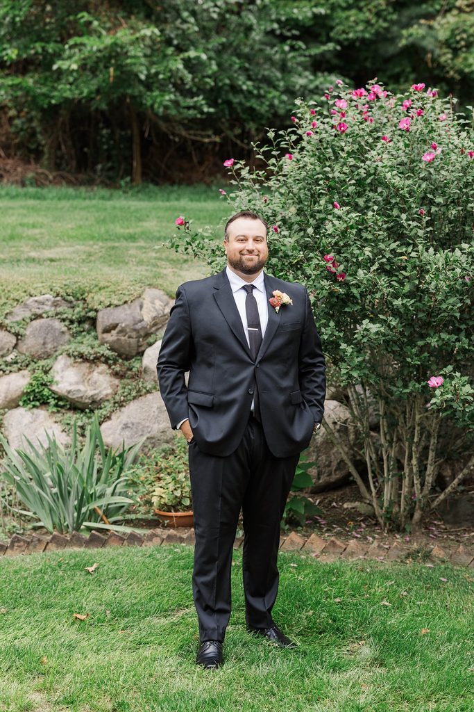 Full-length portrait of Cole wearing a classic black wedding suit and floral boutonniere in the gardens at Black Star Farms in Suttons Bay, Michigan.