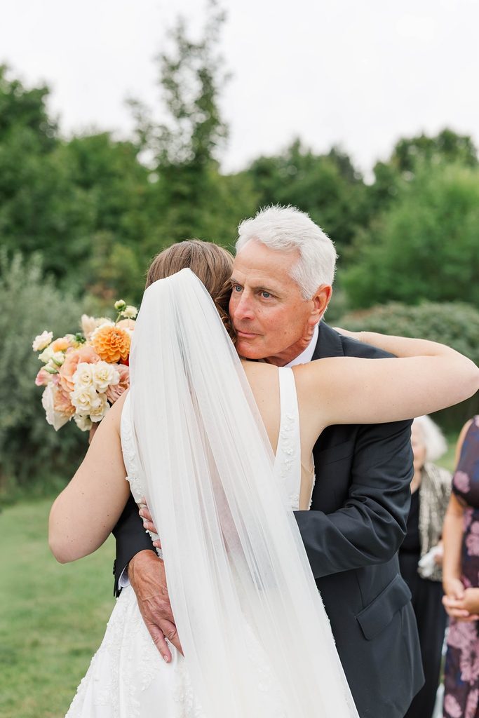 Allison embracing her father at the altar during an emotional moment at her Black Star Farms vineyard wedding ceremony in Suttons Bay, Michigan.
