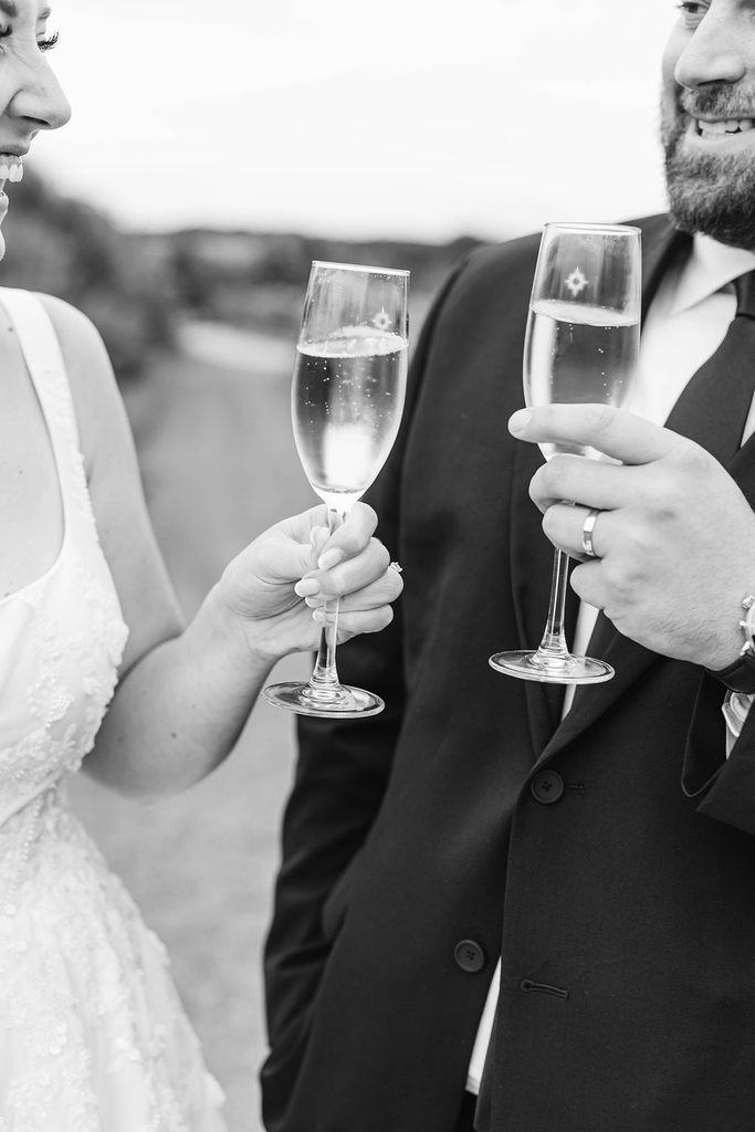 Black-and-white candid photograph of Allison and Cole clinking wine glasses during their wedding celebration at Black Star Farms in Suttons Bay.