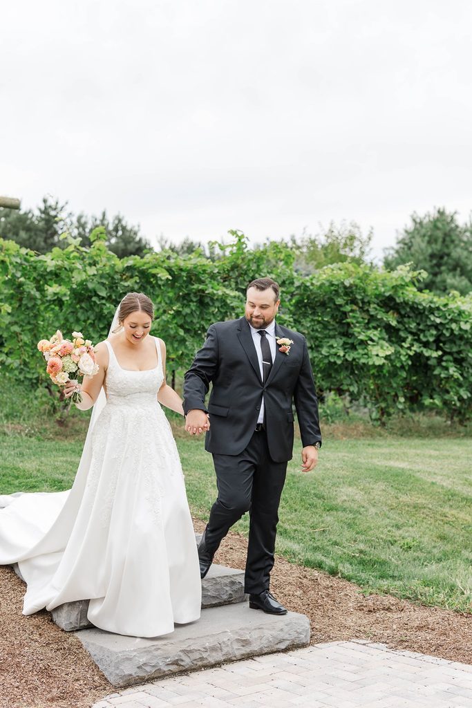 Allison and Cole walking together beside the lush grapevines at Black Star Farms following their intimate Northern Michigan wedding ceremony.