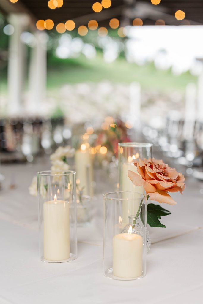 Peach rose centerpiece and glowing pillar candles decorating the wedding reception table at Black Star Farms in Suttons Bay, Michigan.