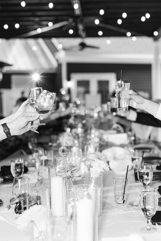 Black-and-white photograph of wedding guests raising their glasses around a long reception table at Black Star Farms in Northern Michigan.