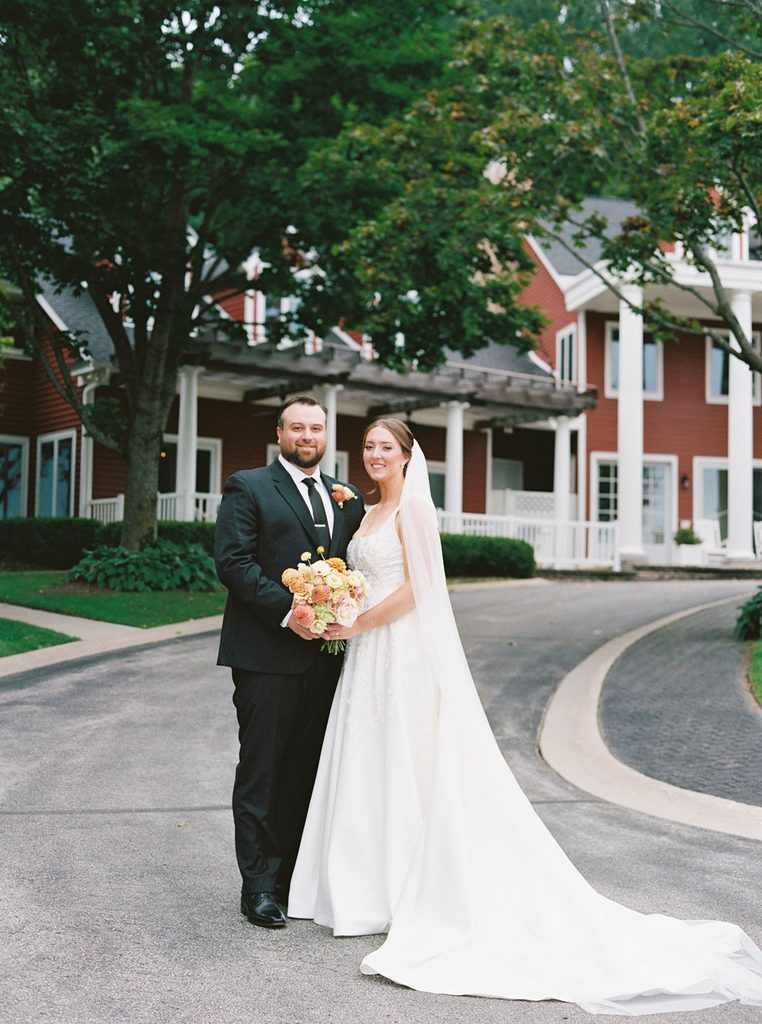 Film photograph of Allison and Cole posing together outside the red Black Star Farms Inn during their intimate wedding in Suttons Bay, Northern Michigan.