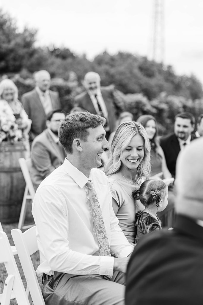 Candid black-and-white wedding photograph capturing a guest's reaction to discovering he was the surprise ring bearer during Allison and Cole's Black Star Farms wedding.