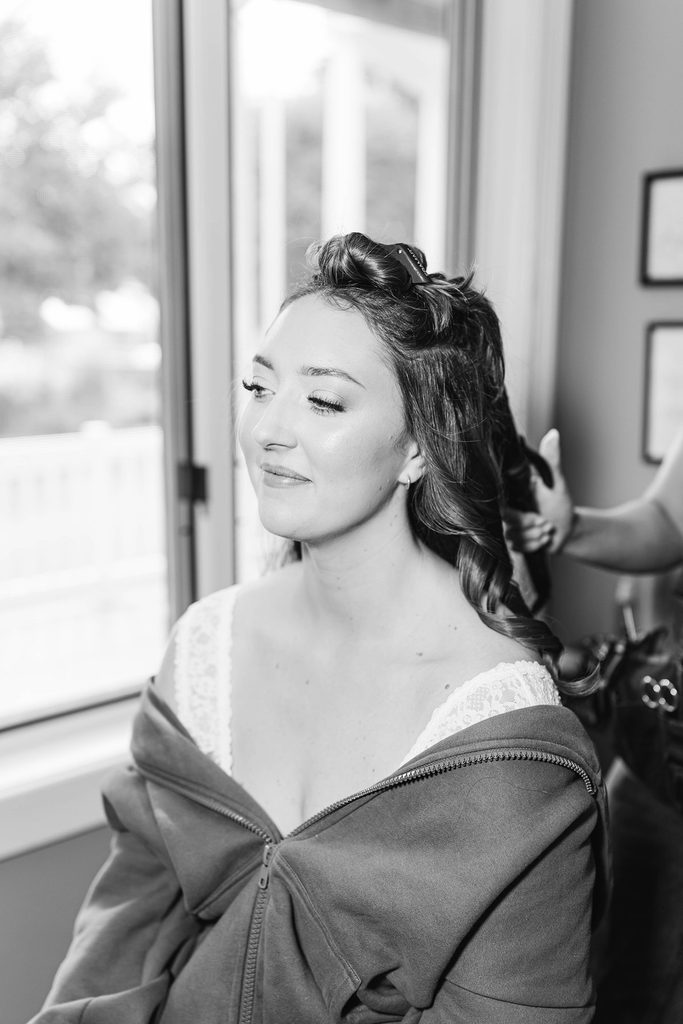 Black-and-white photograph of Allison having her hair styled while getting ready for her Black Star Farms wedding in Suttons Bay, Michigan.