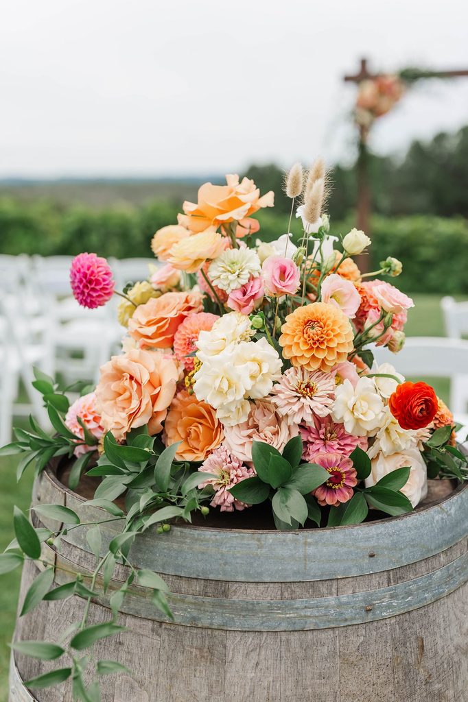 Colorful peach, pink, orange, and cream wedding flowers arranged on a wine barrel by Leelanau Plant Company for a Black Star Farms vineyard ceremony.