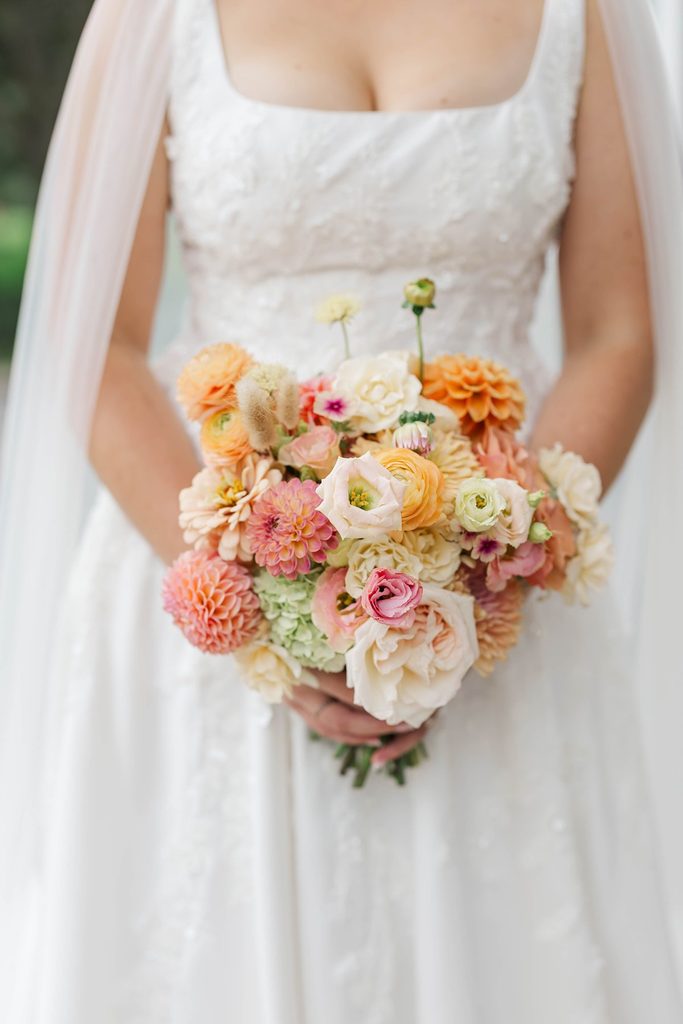 Close-up of Allison holding her colorful bridal bouquet designed by Leelanau Plant Company, featuring peach, pink, and yellow wedding flowers.