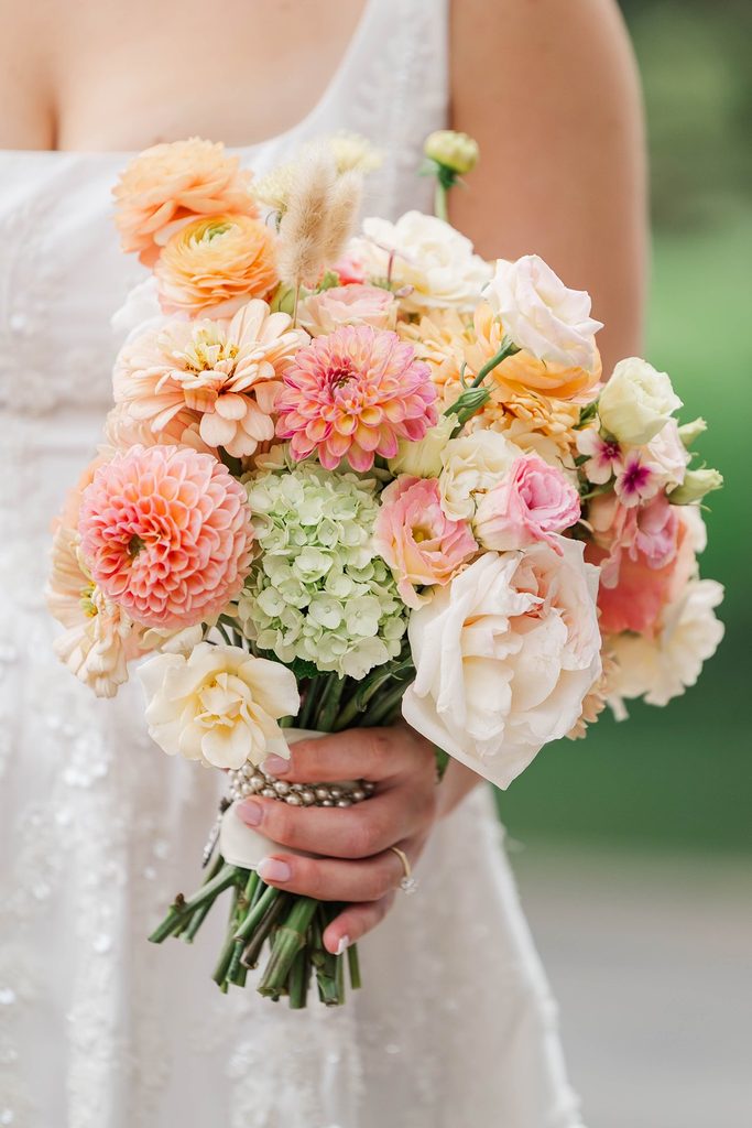 Close-up of Allison's colorful bridal bouquet featuring peach, pink, orange, and cream flowers designed by Leelanau Plant Company.