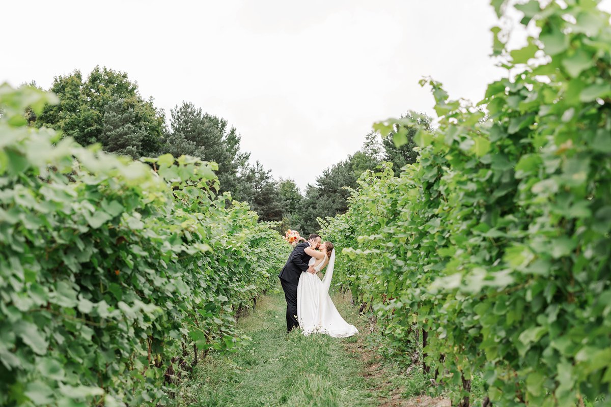 Allison and Cole kissing between vineyard rows during their Black Star Farms wedding in Suttons Bay, Northern Michigan.