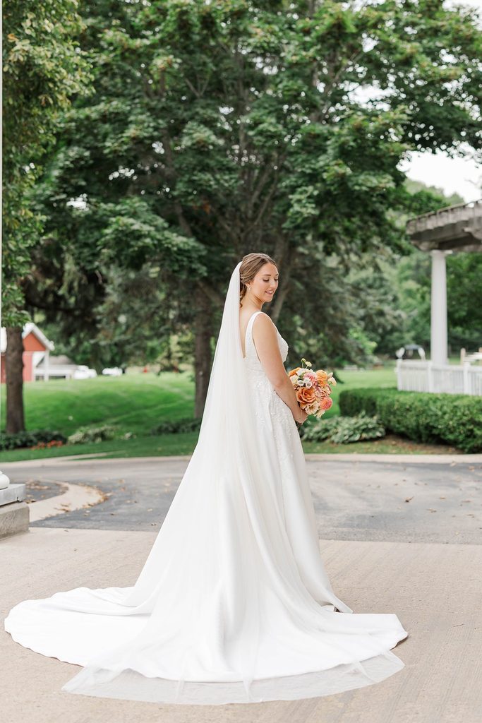 Allison standing outdoors in her wedding gown and veil, holding a colorful bridal bouquet at Black Star Farms in Suttons Bay, Michigan.