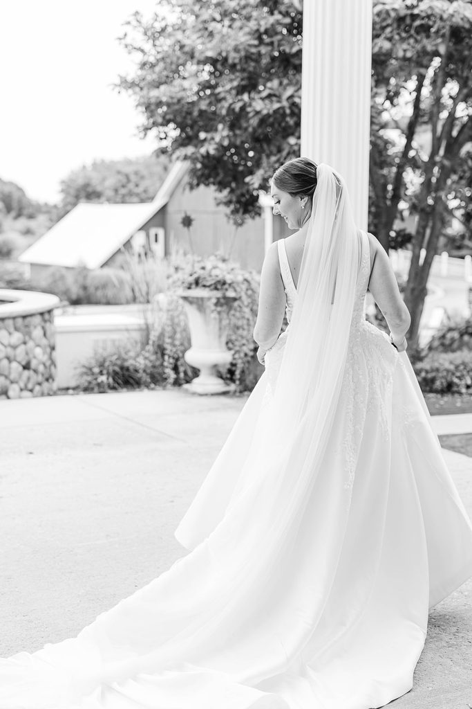 Black-and-white bridal portrait of Allison looking over her shoulder, showing the flowing train and veil of her wedding gown at Black Star Farms.