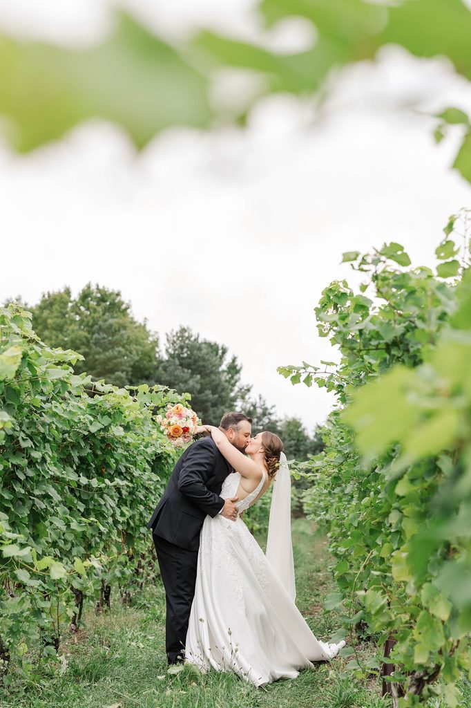 Allison and Cole share a romantic kiss surrounded by lush vineyard rows at Black Star Farms in Suttons Bay, Michigan.