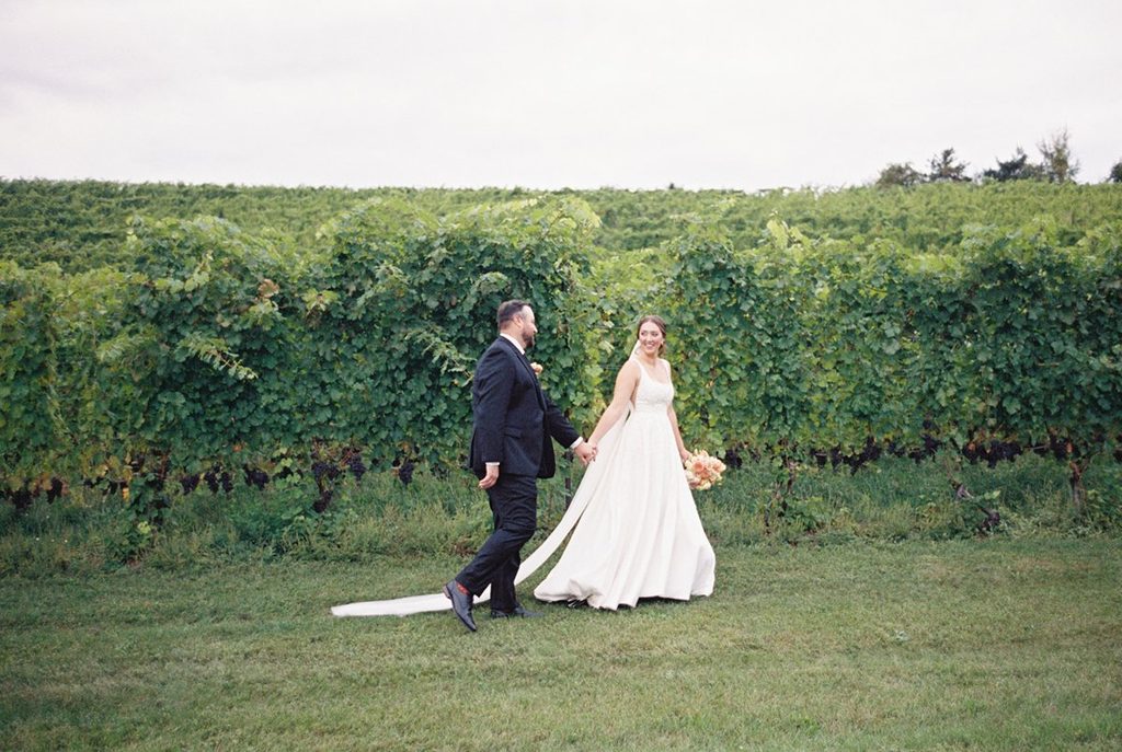 Film photograph of Allison and Cole walking hand in hand beside the vineyard at Black Star Farms during their Northern Michigan wedding.